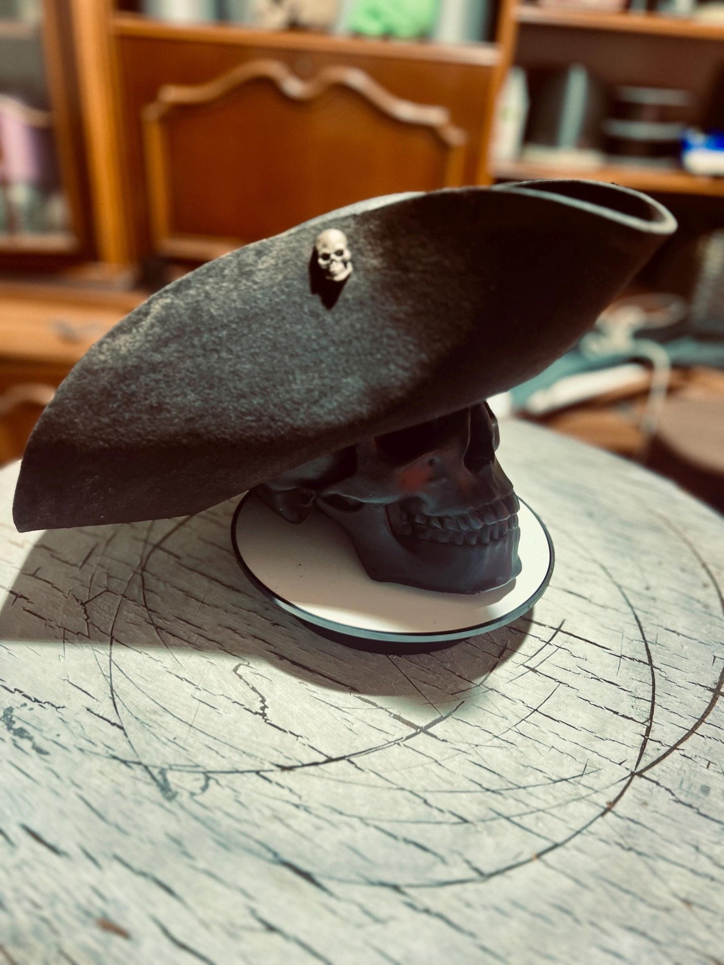 Black artisan pirate hat for adults displayed on a skull stand with a small skull decoration