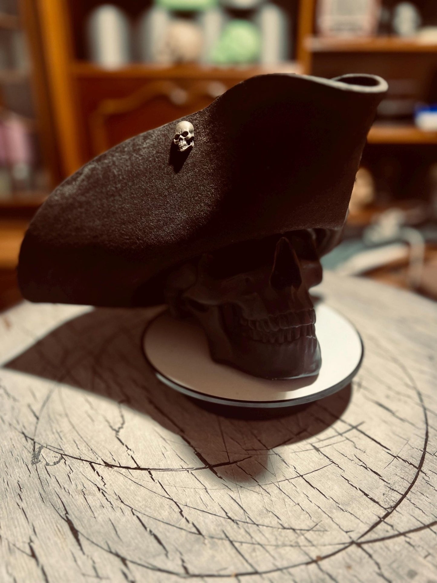 Black artisan pirate hat for adults displayed on a black skull stand with a small skull pin