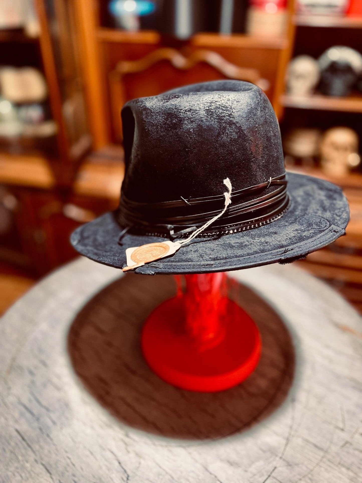 Authentic handcrafted vintage hat in black with decorative leather band and tag on red stand