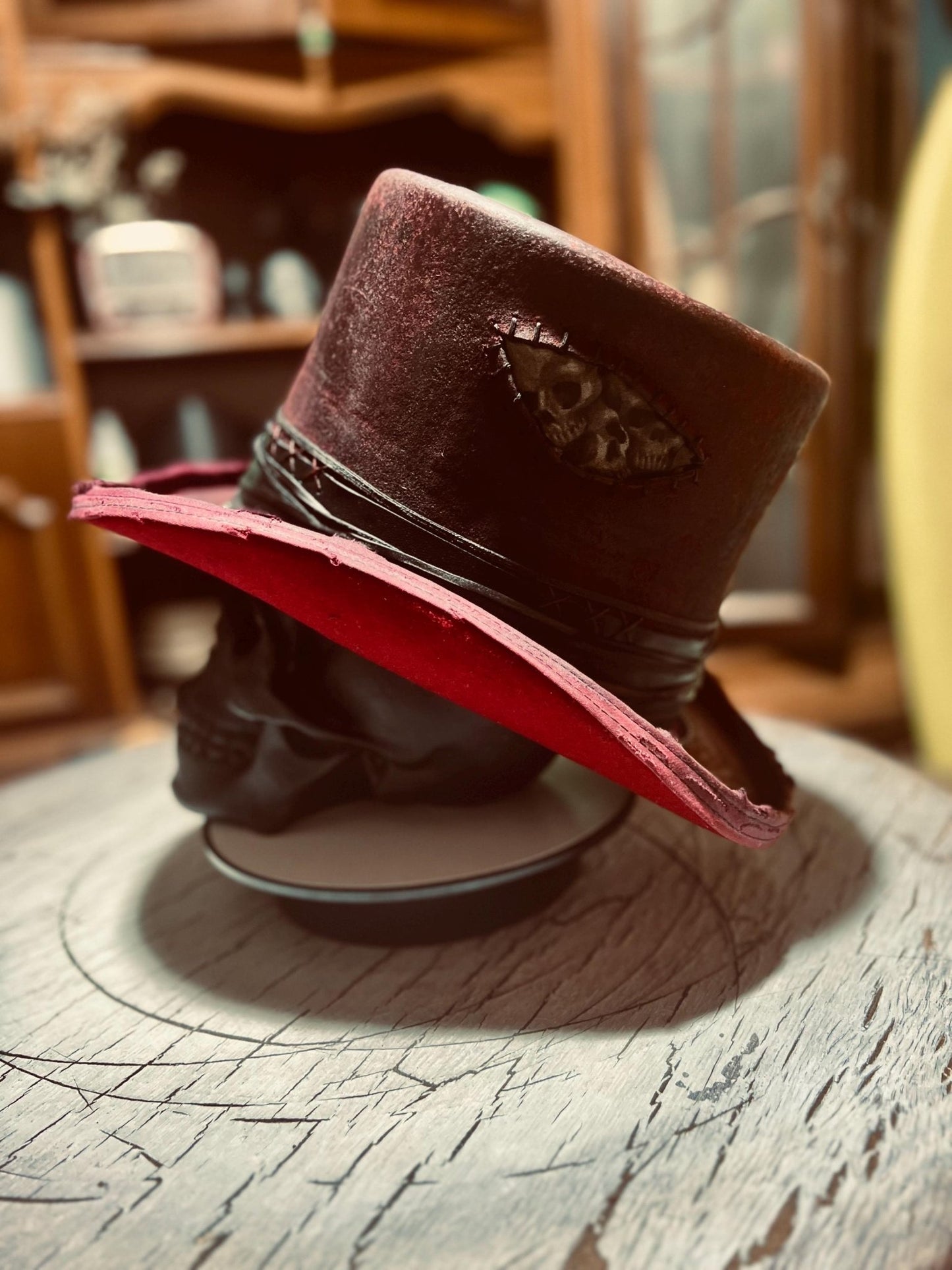 Custom distressed top hat in deep red with a skull patch and black band by JonHats on wooden surface