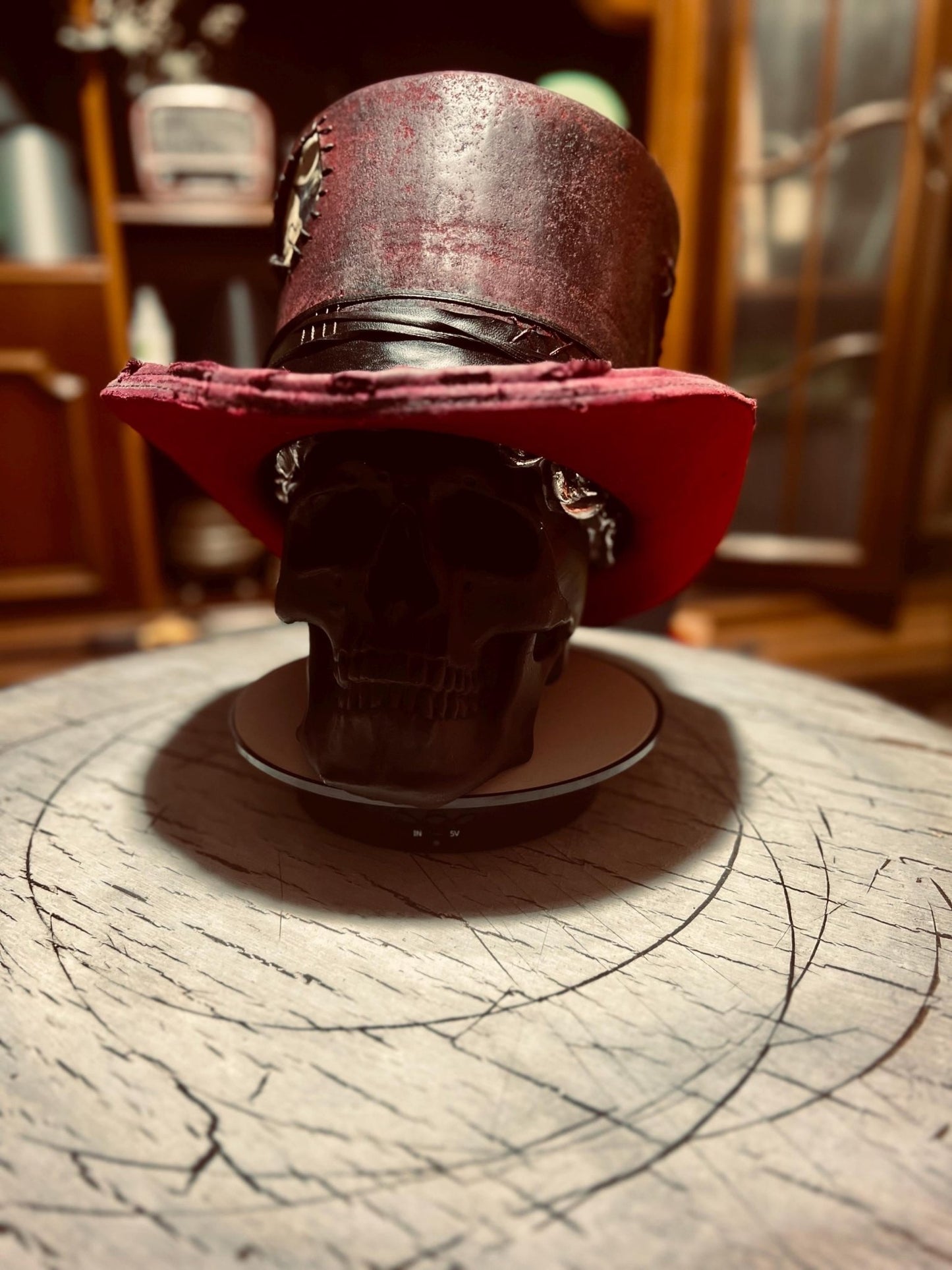 Custom distressed top hat in red with black band displayed on a black skull stand