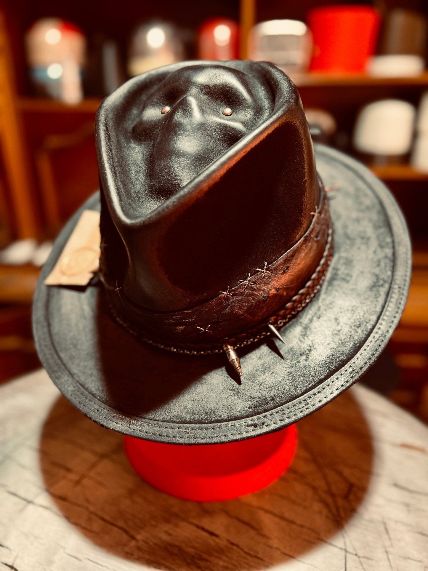 Handcrafted vintage gothic hat in black leather with brown stitched band displayed on red stand