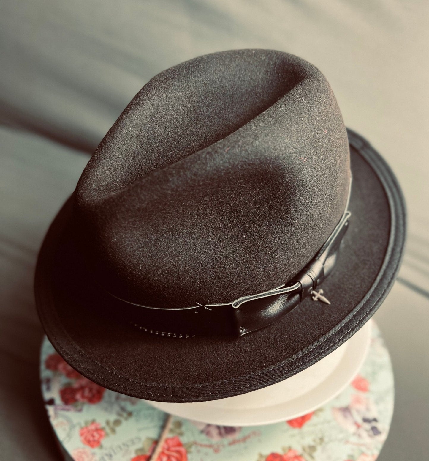 Luxury men's classic fedora in dark brown with leather band by JonHats displayed on floral surface