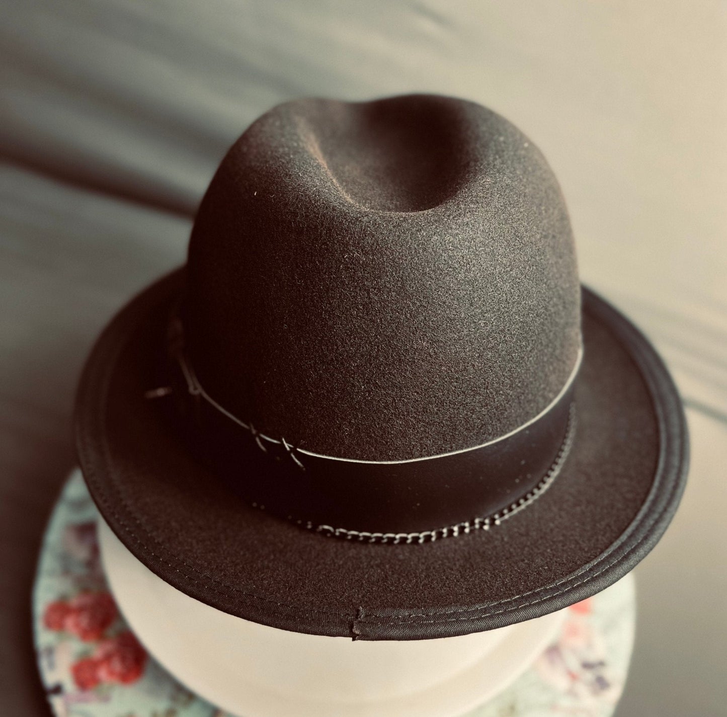 Luxury men's classic fedora in dark felt with black leather band on floral round stand