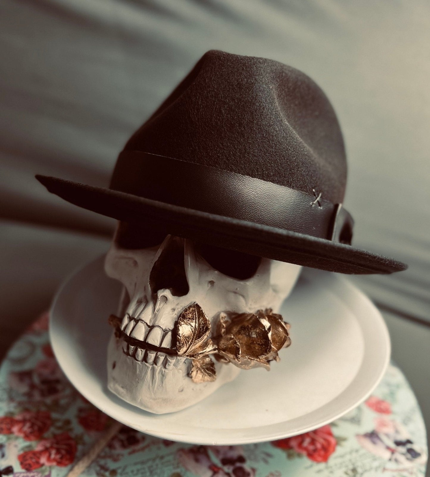 Luxury men's classic fedora in black with leather band displayed on a skull prop holding golden rose