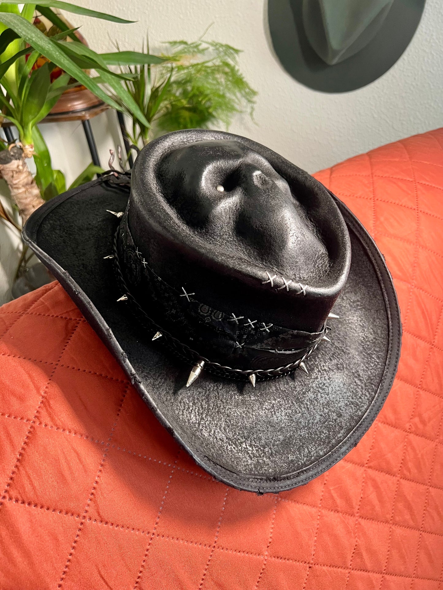 Black skull themed cowboy hat with silver spikes and stitched details by JonHats resting on orange quilted surface