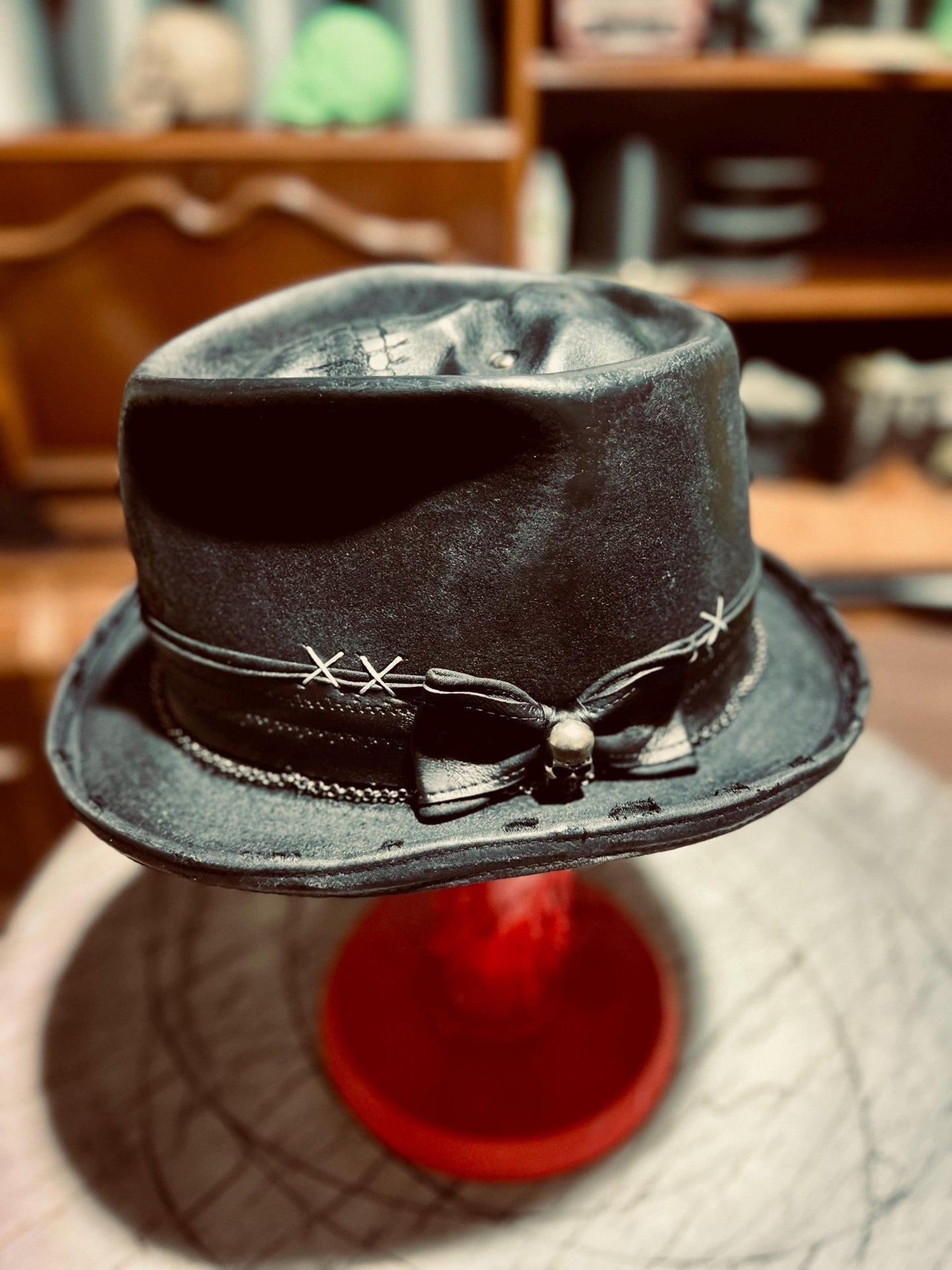 JonHats handmade distressed fedora in black with decorative stitching and leather band on red stand