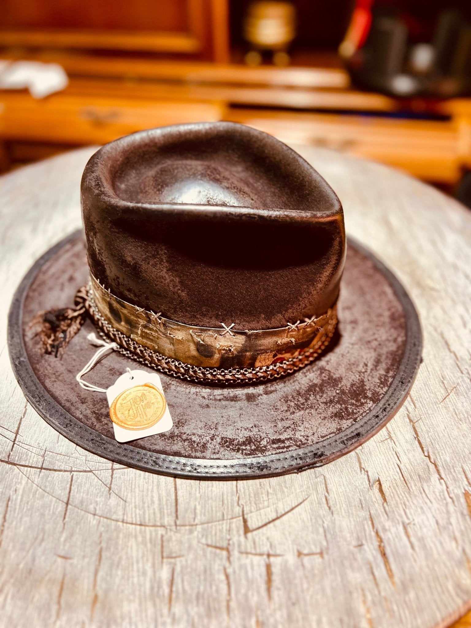 Handmade vintage distressed hat in brown with decorative band on rustic wooden surface by JonHats