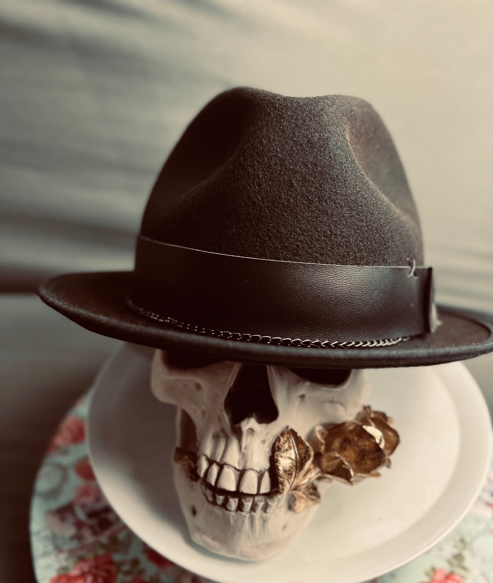 Luxury men's classic fedora in black with leather band displayed on a skull model with a flower in its mouth